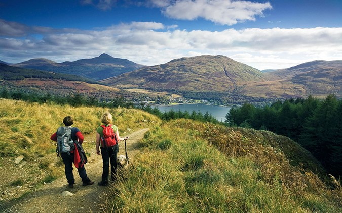 Walkers standing on a hill looking down to crystal clear blue loch